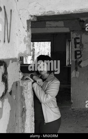 Black and white photo. A young woman standing against the wall in a ruined old building. Stock Photo