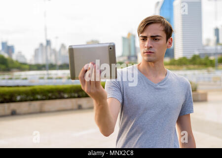 Young handsome man using digital tablet while relaxing at the pa