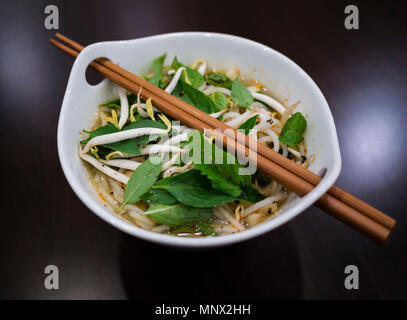 Beautiful and appetizing photo of a traditional vietnamese chicken noodle soup, also know as Pho Ga. In a white bowl with wooden background and luxuri Stock Photo