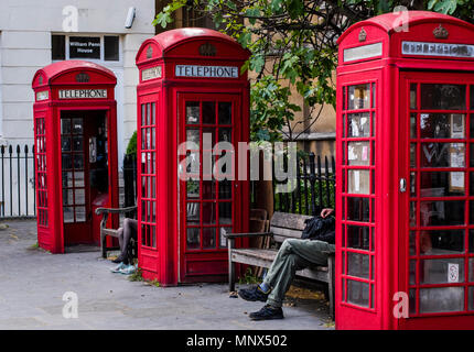 Man and woman, sitting on benches between red telephone boxes, London, England, UK Stock Photo