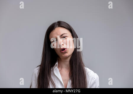 Scornful attractive woman talking to the camera as she jeers at the viewer with a derisory expression and frown over grey with copy space Stock Photo