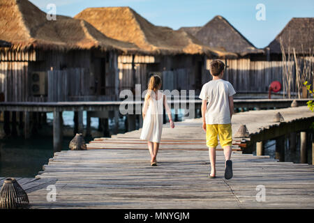 Kids brother and sister walking on wooden footbridge during summer vacation at luxury resort Stock Photo