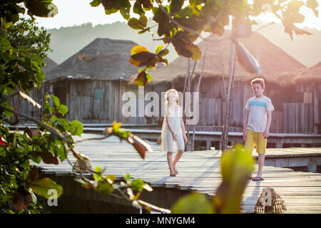 Kids brother and sister walking on wooden footbridge during summer vacation at luxury resort Stock Photo