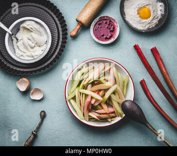 Peeled and sliced rhubarb in bowl on kitchen table background with  with cooking and baking tools, top view. Seasonal food concept.  Rhubarb cake prep Stock Photo
