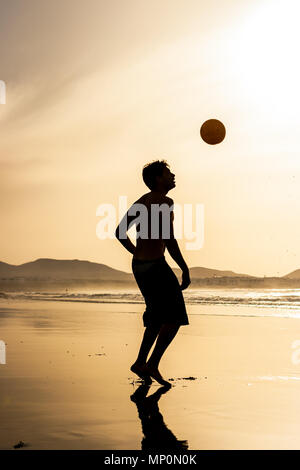Silhouette of a single man playing football (soccer) at sunset. Famara beach, Lanzarote, Canary Islands, Spain. Stock Photo