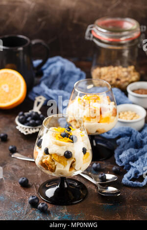 Healthy homemade layered dessert trifle with orange, blueberry, biscuit, yogurt and granola in a glasses Stock Photo