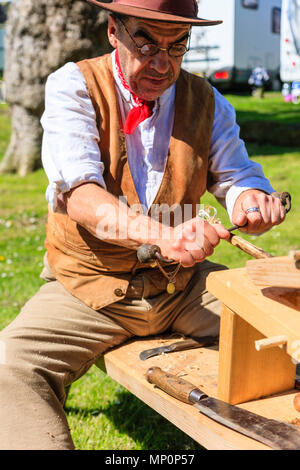 Salute to the 40s popular event. Carpenter, woodworker in 1940's country clothing using a drawknife to shave a wooden pole held on workbench. Stock Photo