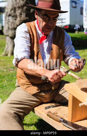 Salute to the 40s popular event. Carpenter, woodworker in 1940's country clothing using a drawknife to shave a wooden pole held on workbench. Stock Photo