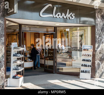 Customers browsing footwear in a branch of Clarks shoe shop in Hamilton, South Lanarkshire, Scotland. Frontage of shop with open door and shoe display