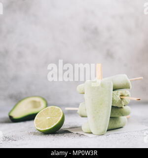 Homemade raw vegan avocado lime popsicle. Sugar-free, non-dairy green ice cream on gray cement textured background. Copy space. Ideas and recipes for healthy snack, dessert or smoothie Stock Photo