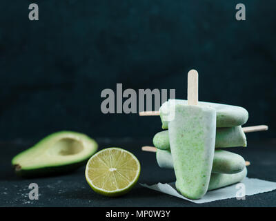 Homemade raw vegan avocado lime popsicle. Sugar-free, non-dairy green ice cream on black textured background. Copy space. Ideas and recipes for healthy snack, dessert or smoothie Stock Photo