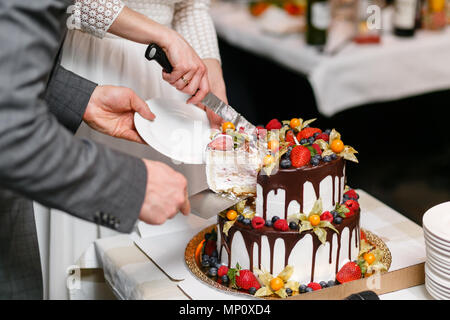 Wedding cake with berries on wooden table. Bride and groom cut sweet cake on banquet in restaurant. piece Stock Photo