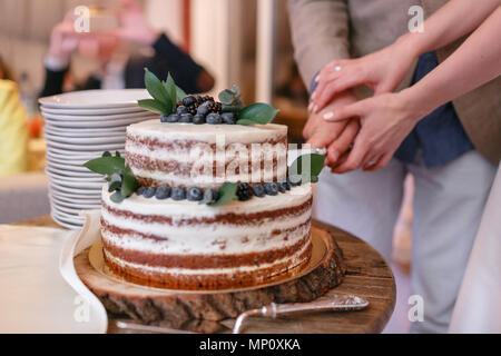 Wedding cake with berries on wooden table. Bride and groom cut sweet cake on banquet in restaurant. Stock Photo