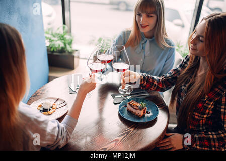 Portrait of three girlfriends holding beverages in glasses. Young women celebrate event in cafe Stock Photo