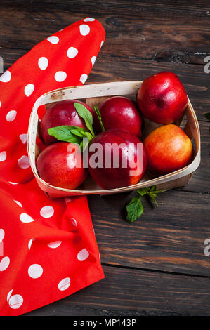 Ripe nectarines lying in a wicker basket on wood background. Stock Photo