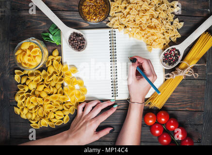 Female hands writing notepad. spices, pasta and vegetables around notebook on wooden table. Mockup. Stock Photo