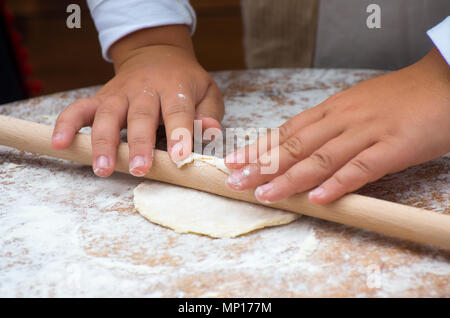 Child hands rolling dough with rolling pin on wooden table Stock Photo