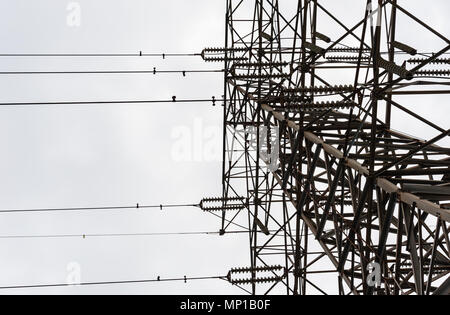 Looking up along large metal electrical transmission tower with parallel insulators and wires against overcast sky. Stock Photo