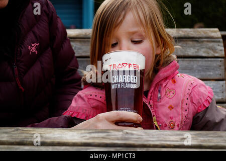 A little girl (3 yr old) tasting from a pint of Trooper beer, made in collaboration with British heavy metal group Iron Maiden Stock Photo