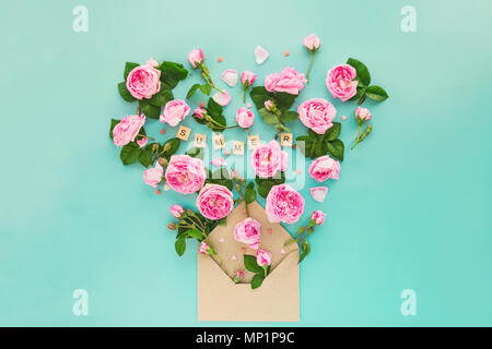 Creative layout with pink tea rose flowers, leaves fly out of croped craft paper envelope in shape of heart on the light turquoise background. Word Summer lettering by wooden letters. Space for text. Stock Photo