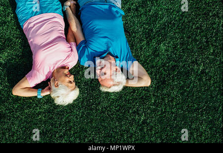 Senior couple laying in grass, top view. Elderly man and woman lying on grass together and hold their hands Stock Photo