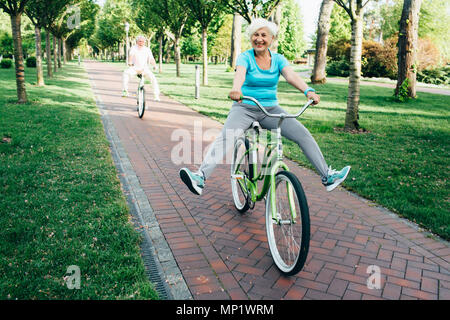 happy senior couple riding their bikes on the park, funny lifting their legs up Stock Photo