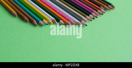 Very used pencils of different colors isolated on a green background Stock Photo