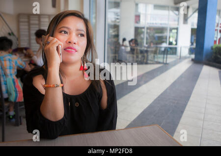 Attractive Asian woman from the Philippines talking on her smartphone indoors. Stock Photo