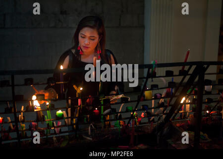 Attractive, upscale Filipino Asian woman lights votive candles in a Catholic church in the Philippines. Stock Photo