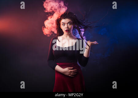 close-up of a young woman with dreadlocks in a black sweatshirt in a big cutout and a burgundy skirt is fun posing and is surprised on a black isolate Stock Photo