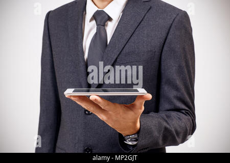 Businessman holds digital tablet against gray background. Stock Photo