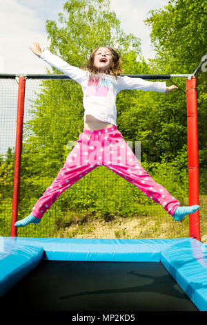 Happy girl jumping high on a trampoline on a sunny day outdoors. Stock Photo