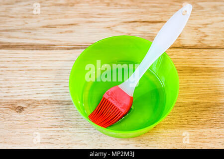 Close up bright red silicone pastry brush in green bowl with oil Stock Photo
