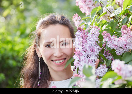Young pretty woman with nice earrings posing near brunches of blooming lilac Stock Photo