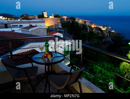 Table with bottle of white wine, two glasses and fruits on balcony with beautiful view on sea and Stari Grad at twilight scene. Romantic celebration o Stock Photo