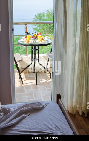 Hotel room with fresh delicious breakfast with pastry, coffee, orange juice and fruits served on the balcony with sea view in the green location. Plac Stock Photo