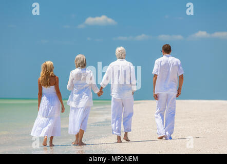 Rear view of four people, two seniors, couples or family generations, holding hands, walking on an empty tropical beach Stock Photo