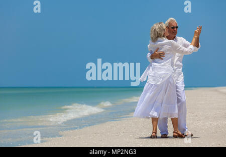 Happy senior man and woman couple dancing and holding hands on a deserted tropical beach with turquoise sea and clear blue sky Stock Photo