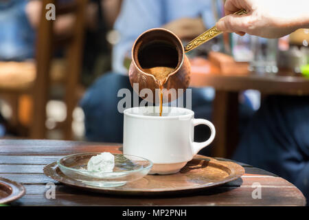 Woman hand pouring greek coffee from a copper pot on a white cup placed on a tray with loukumi Stock Photo