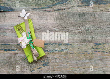 Green napkin, vintage cutlery and spring flowers on the background of an old wooden table with space for text Stock Photo