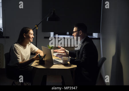 Colleagues working late hours in office discussing business plan Stock Photo