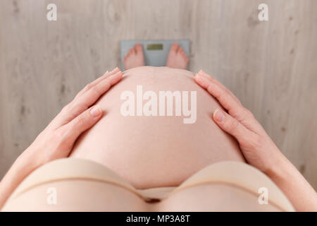 closeup pregnant woman standing on scales top view. Controlling weight gain on pregnancy time Stock Photo