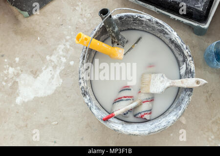 Close-up dirty bucket with used brushes and paint rollers soaked in muddy water. Top view. Construction site and house renovation concept Stock Photo