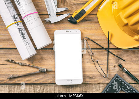 Architect workplace. Smart phone with white blank screen, project construction blueprints and engineering tools on wooden desk, top view, space for te Stock Photo