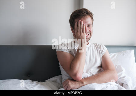 Caucasian man sitting in bed in the early morning, He is happy and smile closing his face. Stock Photo