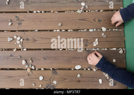 Top view of child's hands playing with stones on woodden bench, desk outdoors at playground, closeup, no recognizable people, no people Stock Photo