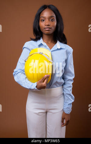 Young beautiful African Zulu businesswoman with hardhat against  Stock Photo