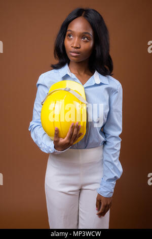 Young beautiful African Zulu businesswoman with hardhat against  Stock Photo