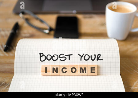 Closeup on notebook over wood table background, focus on wooden blocks with letters making Boost your income text. Stock Photo