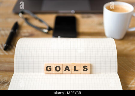 Closeup on notebook over wood table background, focus on wooden blocks with letters making GOALS word. Business concept image. Stock Photo